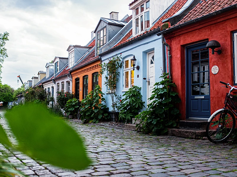 En charmerende brostensbelagt gade med farverige rækkehuse og grønne planter langs facaderne