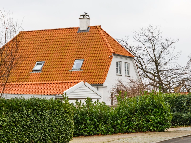 Hvid murermestervilla med orange tag og hæk omkring