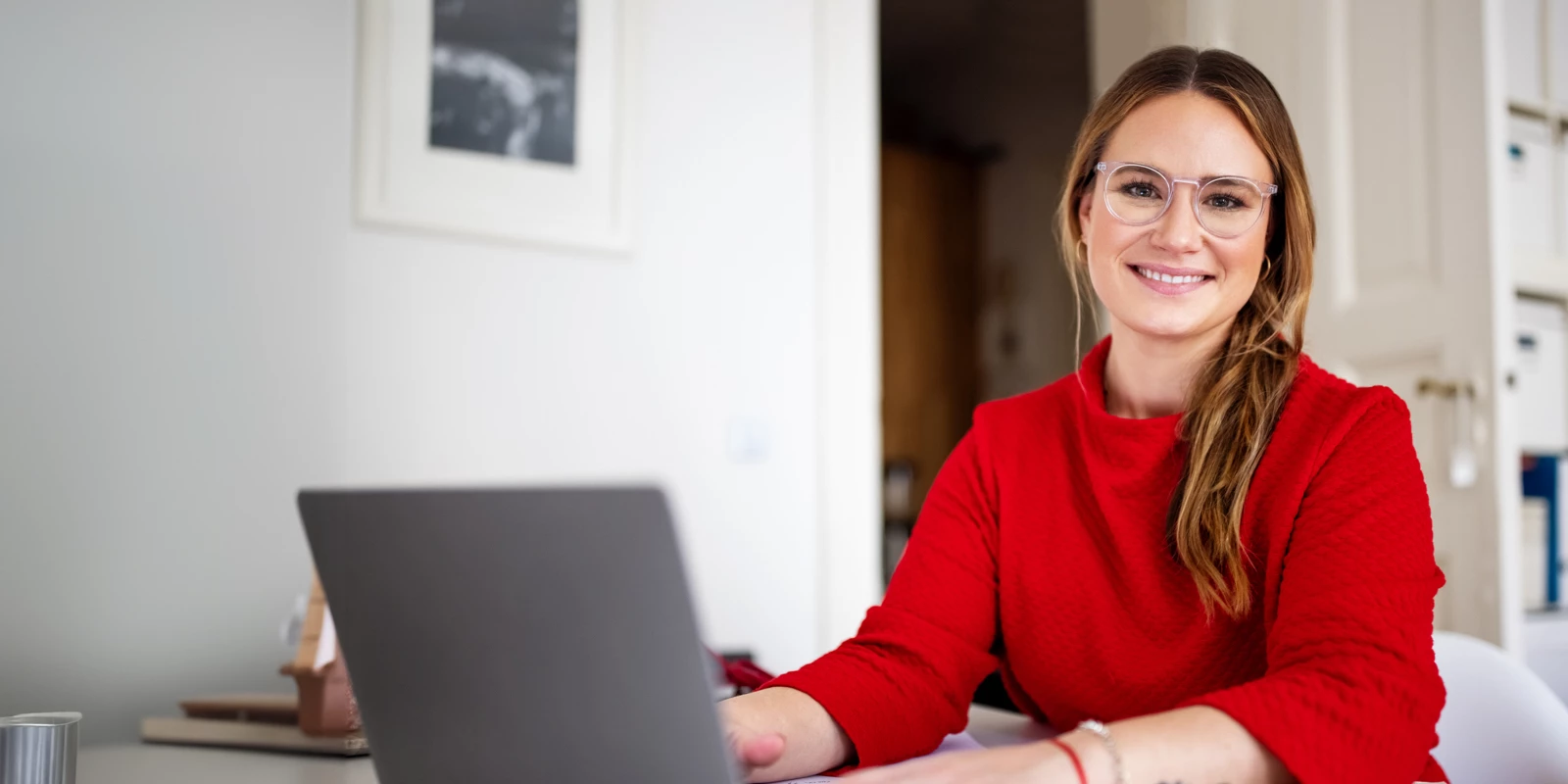 Kvinde i rød trøje med briller ved en computer