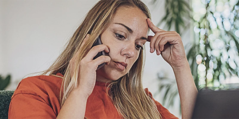 Kvinde i orange trøje sidder bekymret og taler i telefon