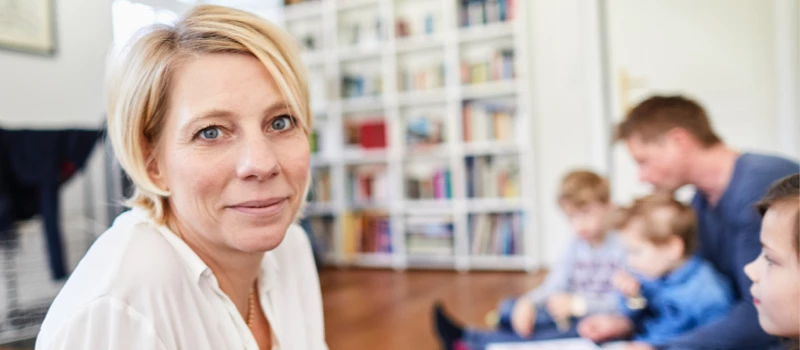 Blond dame med to børn og en mand i baggrunden