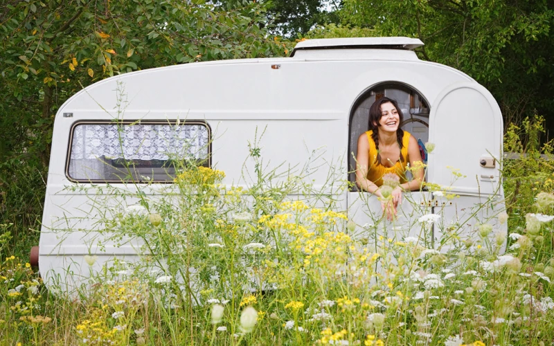 En campingvogn i naturen med smilende kvinde i gul kjole