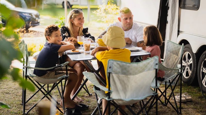 Familie på fem spiser frokost ved campingbord