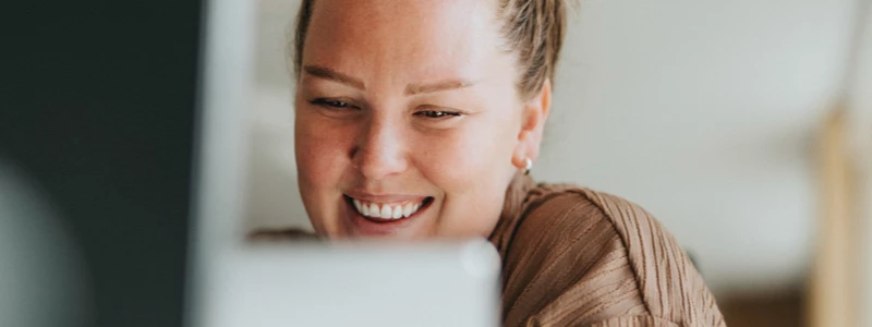 smilende ung kvinde sidder og kigger i en computerskærm