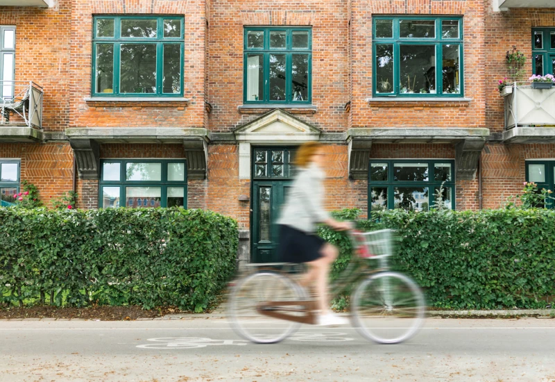 rødhåret Kvinde der cykler hurtigt forbi hus