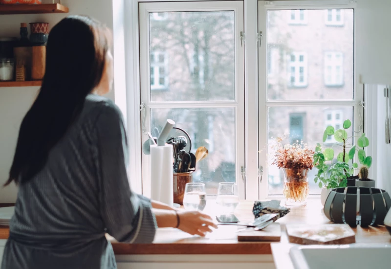 Kvinde i sit køkken der kigger ud af vindue