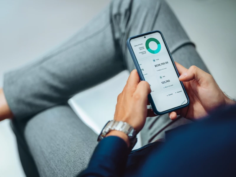 Mand med krydsede ben der kigger på aktier på mobil