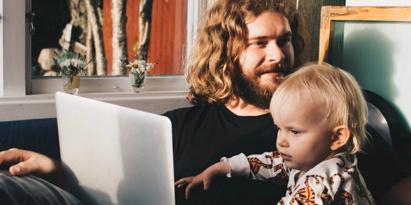 Mand og sit barn der sidder i stue med computer på skød