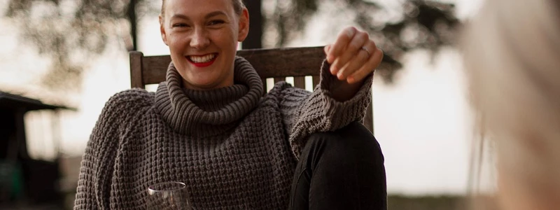 Glad kvinde sidder i stol udenfor med et glas vin i hånden