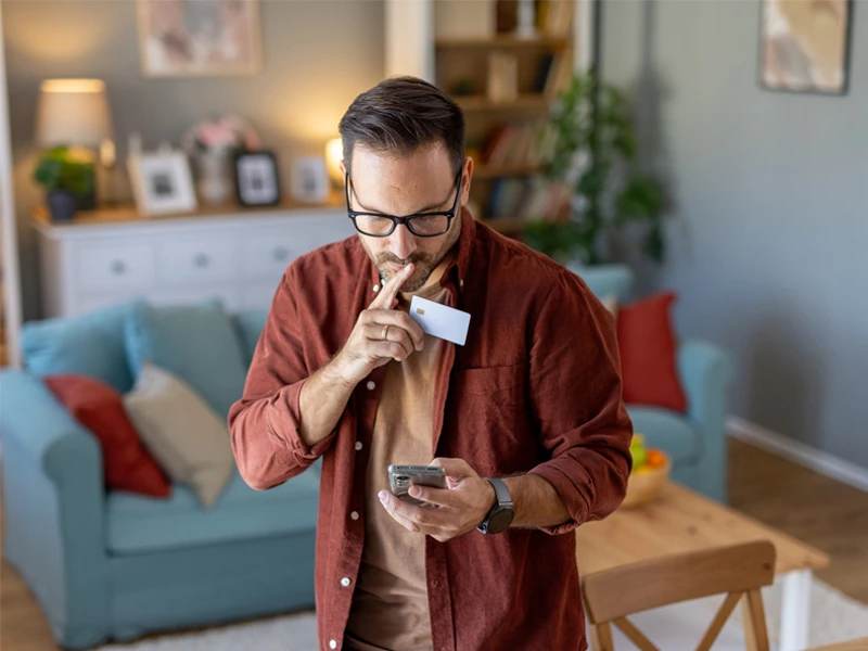 mand der ovevejer køb med telefon i den ene hånd og kreditkort i anden