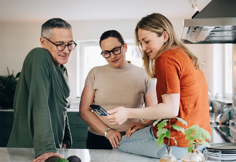 datter, mor og far kigger på datters opgørelse i køkken