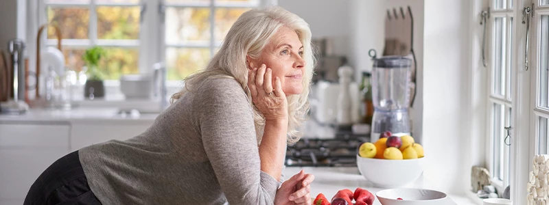 Ældre kvinde der kigger ud af vinduet i sit køkken