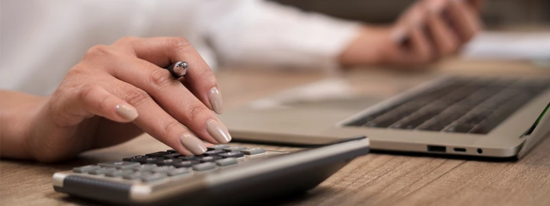 nærbillede af fingre og lommeregner med computer i baggrunden