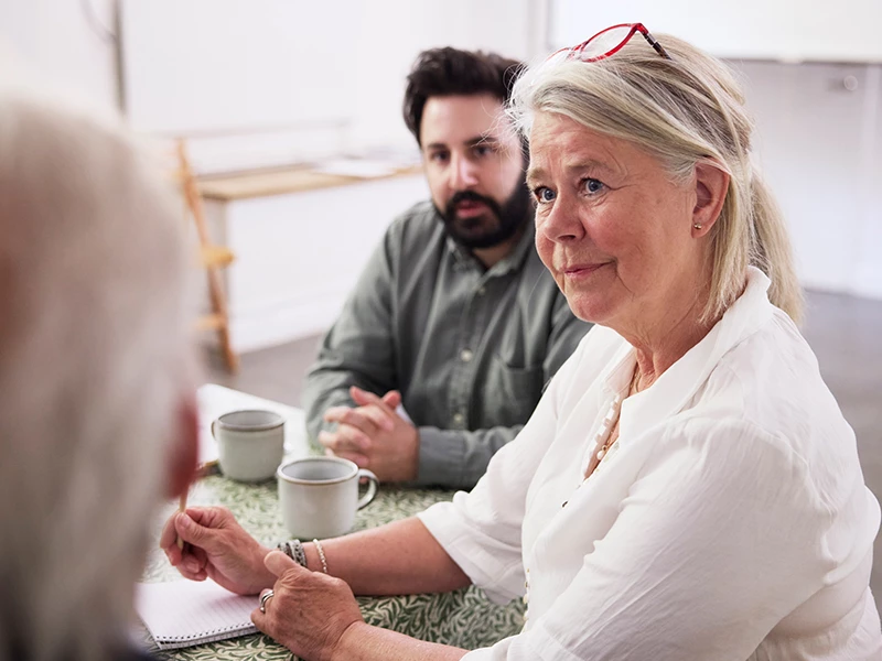 Ældre kvinde og yngre mand ved bord der kigger nysgerrig på ekspert