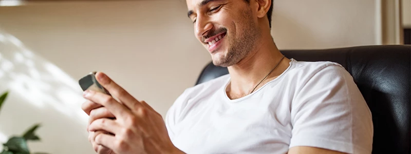 Glad mand med mobil siddende i sort stol