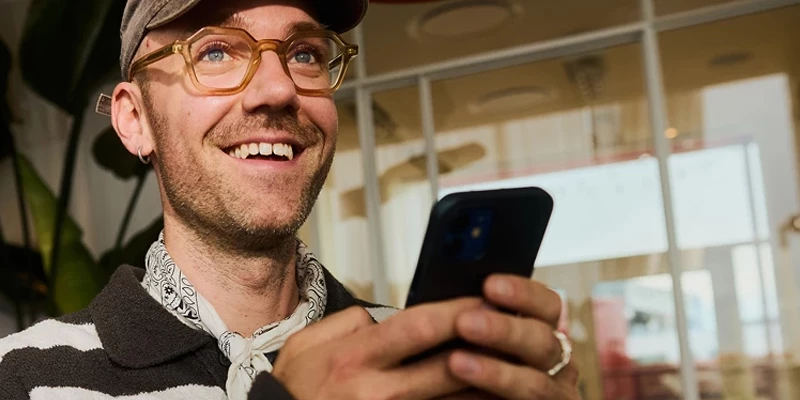 Glad mand med kasket, briller og en mobil i hånden