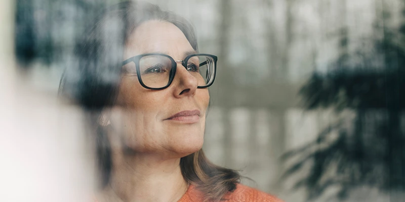 Kvinde med briller kigger ud af vindue