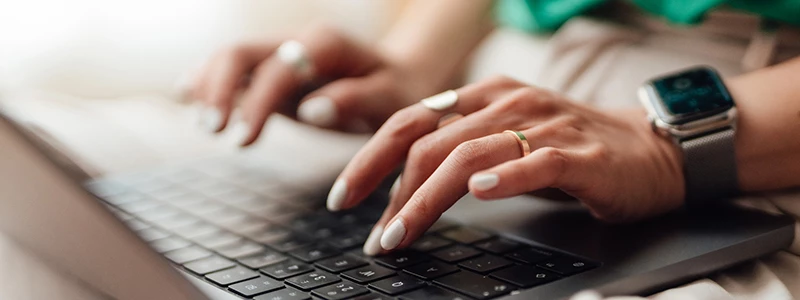 Kvindehænder med hvide negle og ur på venstre håndled på computertastatur