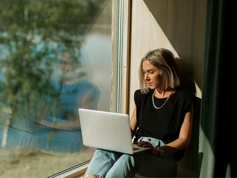 Ung kvinde siddende i vindue med computer på skødet