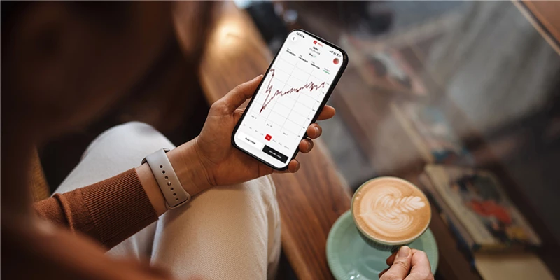 Kvinde med coop bank investering app i den ene hånd og kaffe i den anden hånd