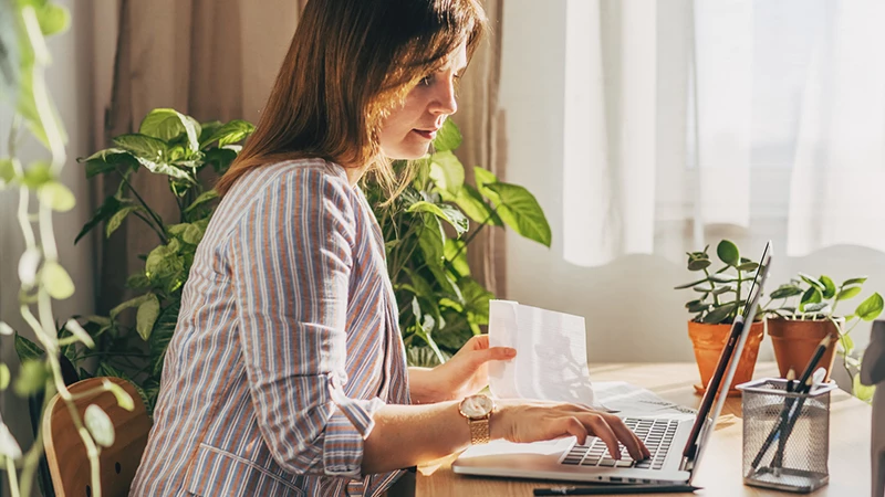 Ung kvinde foran computer i stue med planter i bagrunden