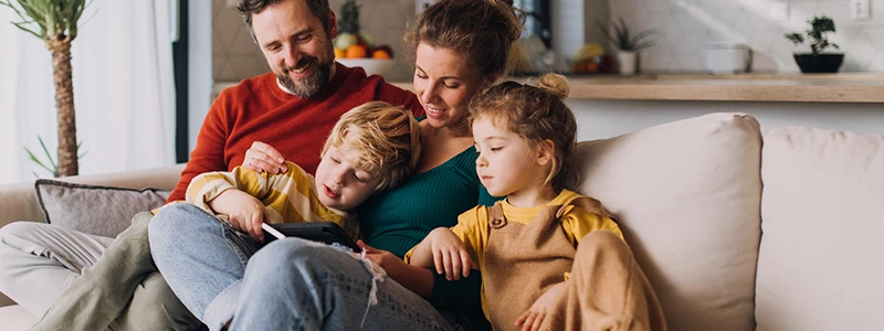 Familie på fire i sofaen i færd med at kigge på mobilskærm