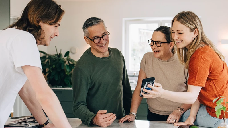 familie i køkken kigger på mobil i godt humør
