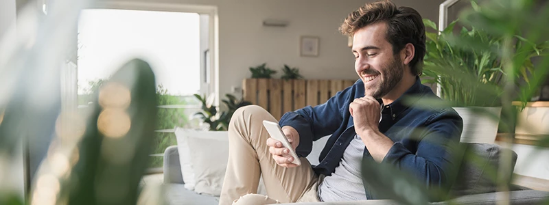 mand i skjorte og beige bukser kigger på mobil med planter sløret i forgrund