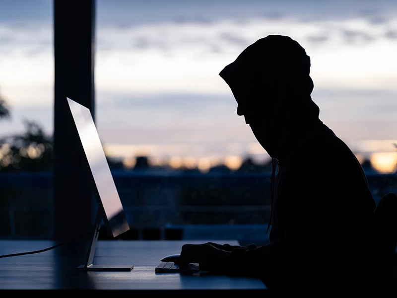 Hacker med hoodie foran stationær computer i mørkbelagt rum