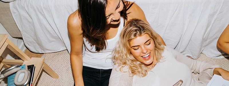 2 yngre kvinder kvinder siddende på gulvet med mobil i den ene kvindes hånd