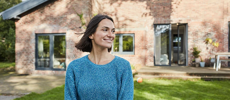 glad kvinde udenfor i sin have med hus i baggrunden