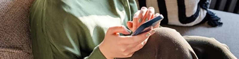 kvinde med grøn trøje taster på sin mobil i sofa