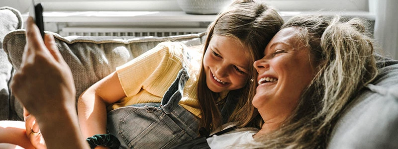 datter og mor ligger i sofa og kigger på mobil sammen
